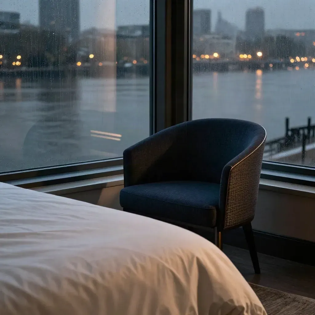 Thames-view suite window at night with river reflections, navy chair, and folded duvet